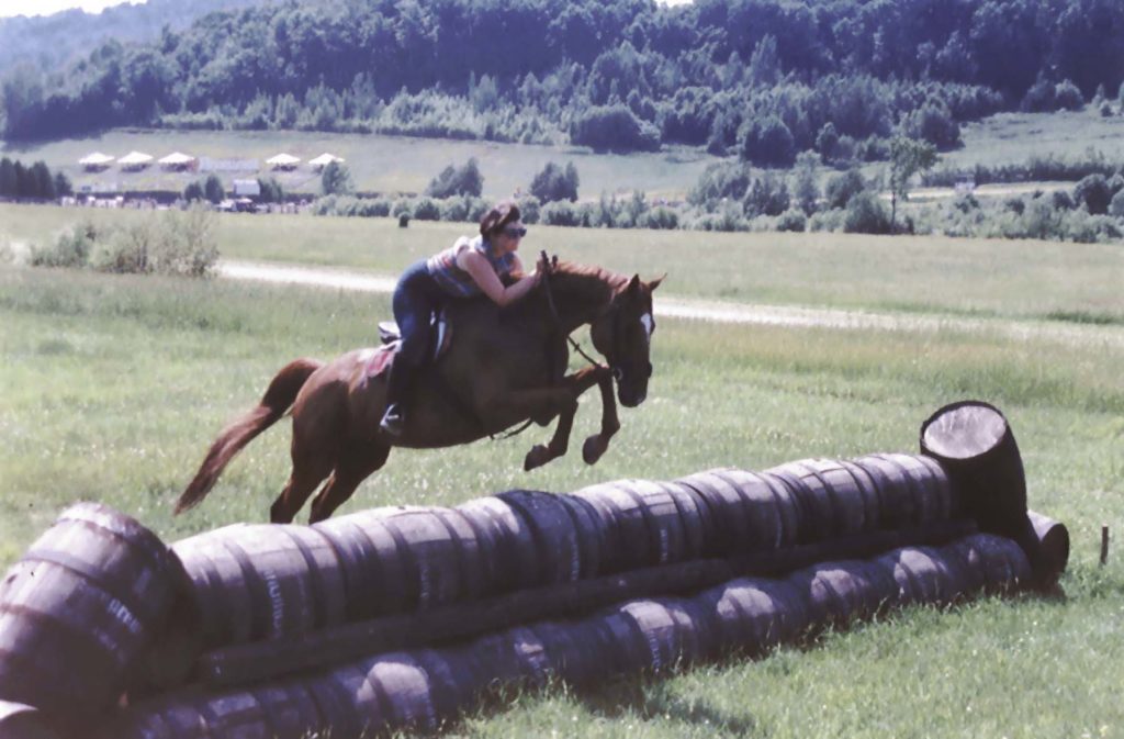 Geneviève Benoit jumping a row of barrels on a chestnut horse on the Bromont cross-country course