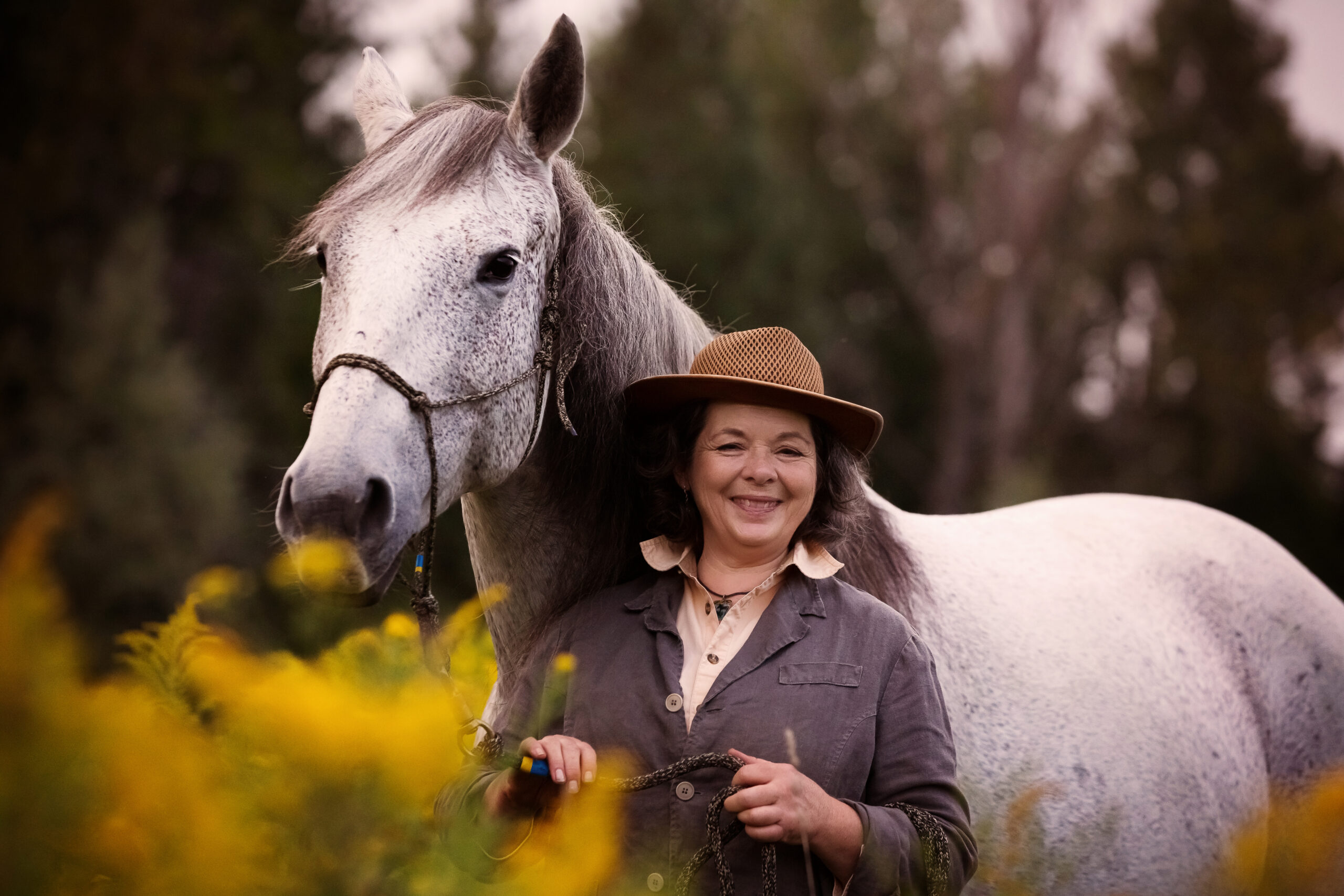 Geneviève Benoit avec un cheval gris dans un champ de verges d'or