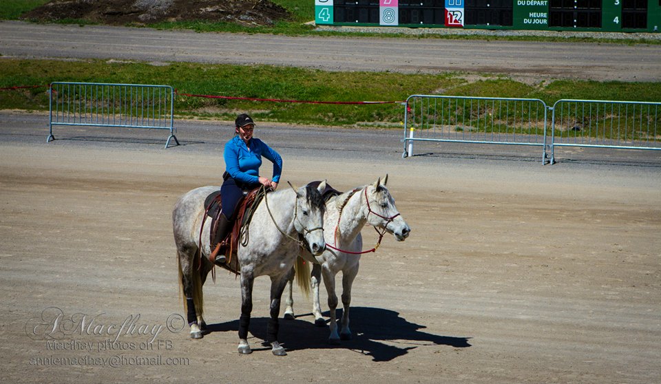 Geneviève Benoit en selle avec deux chevaux sur une piste d'hippodrome